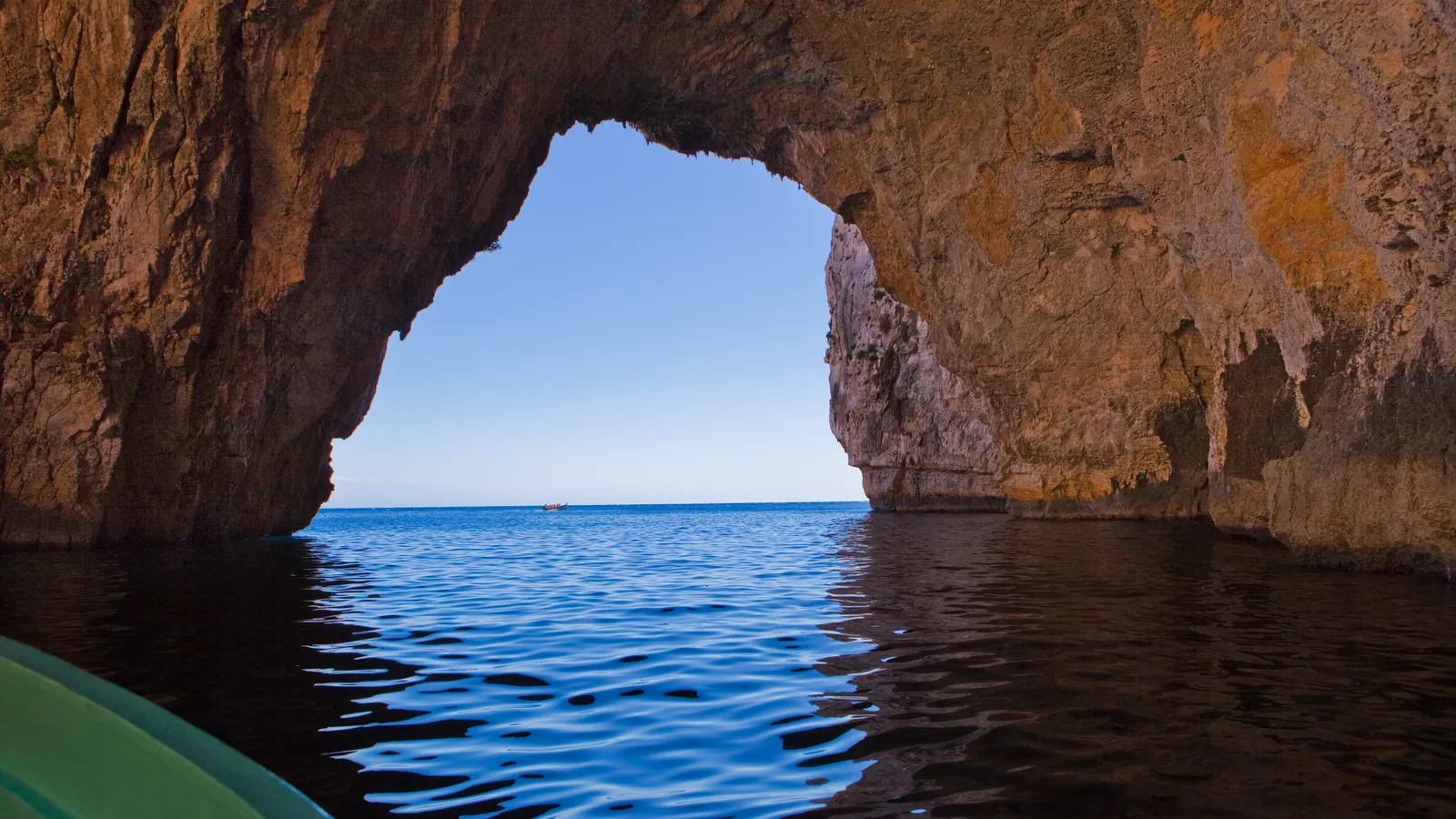 Blick aus dem Boot durch den Felsbogen der Blauen Grotte auf Malta auf das tiefblaue, ruhige Meer