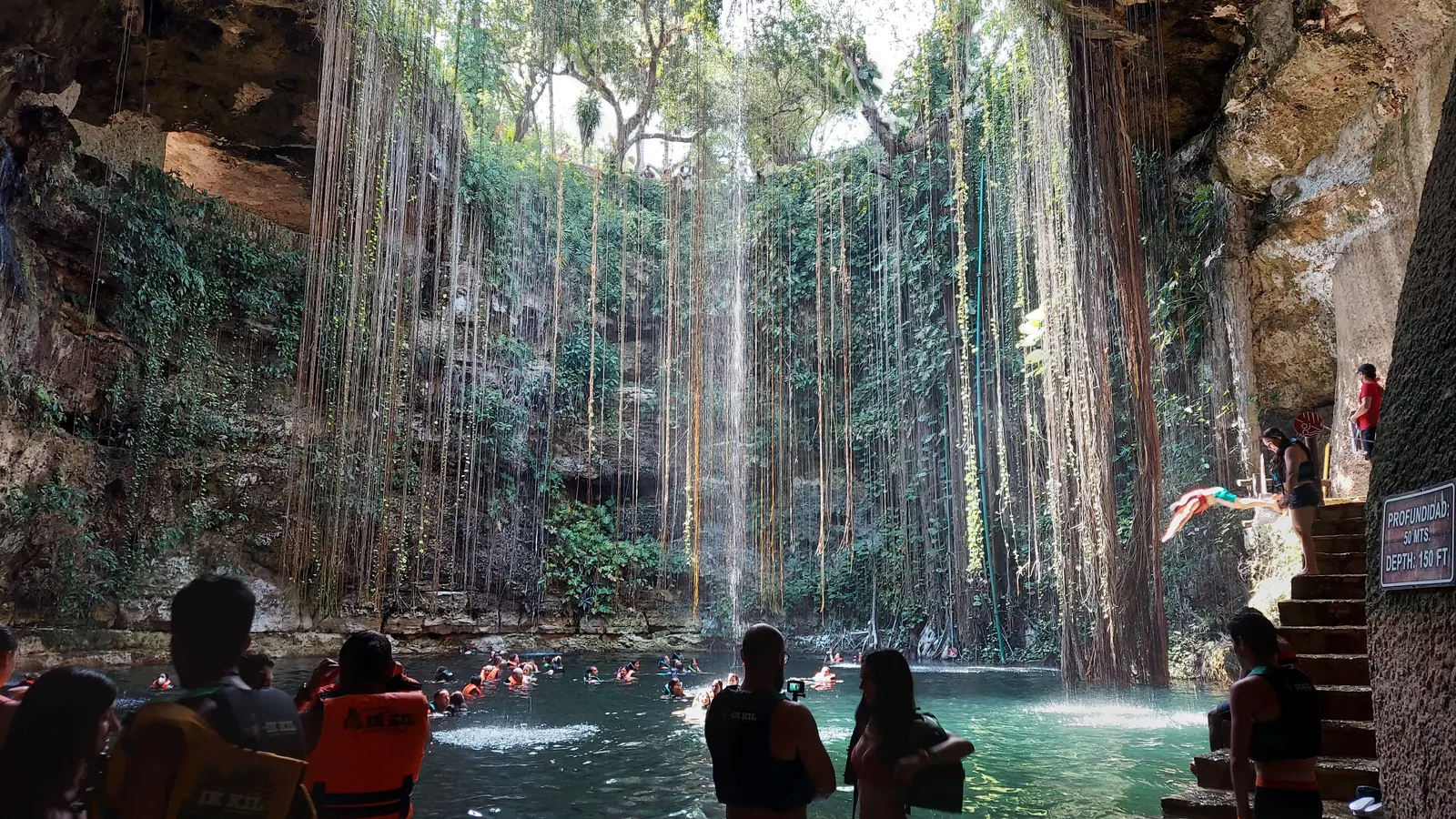 Schwimmer im runden Wasserbecken der Cenote Ik Kil, von oben hängen Luftwurzeln herab