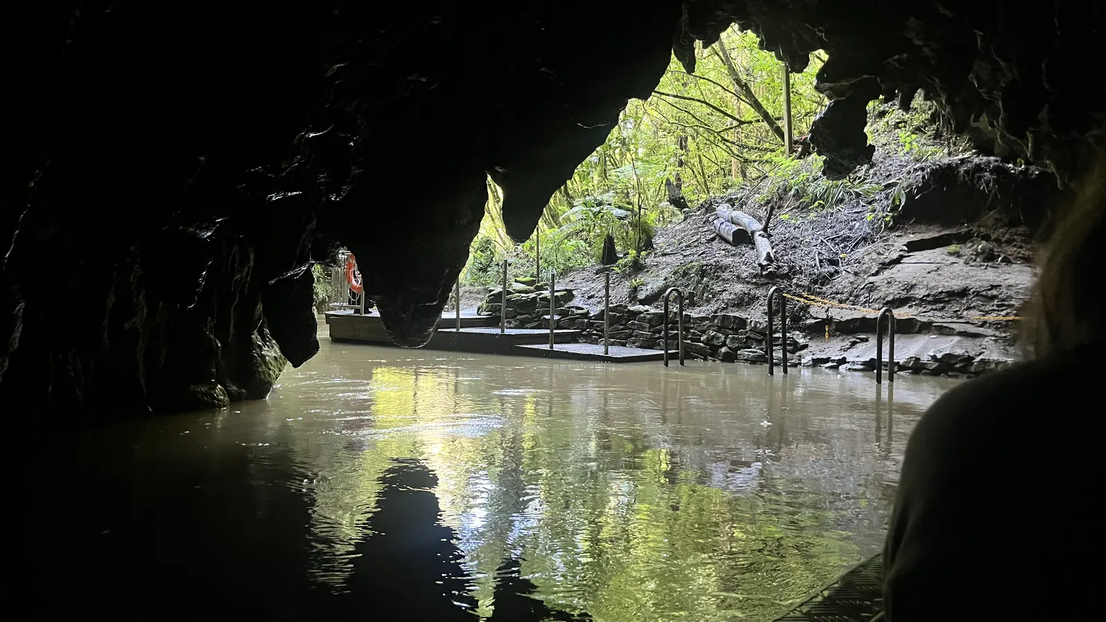 Höhlenausgang der Waitomo-Höhlen über dem Wasser, Steg und Geländer am Ufer
