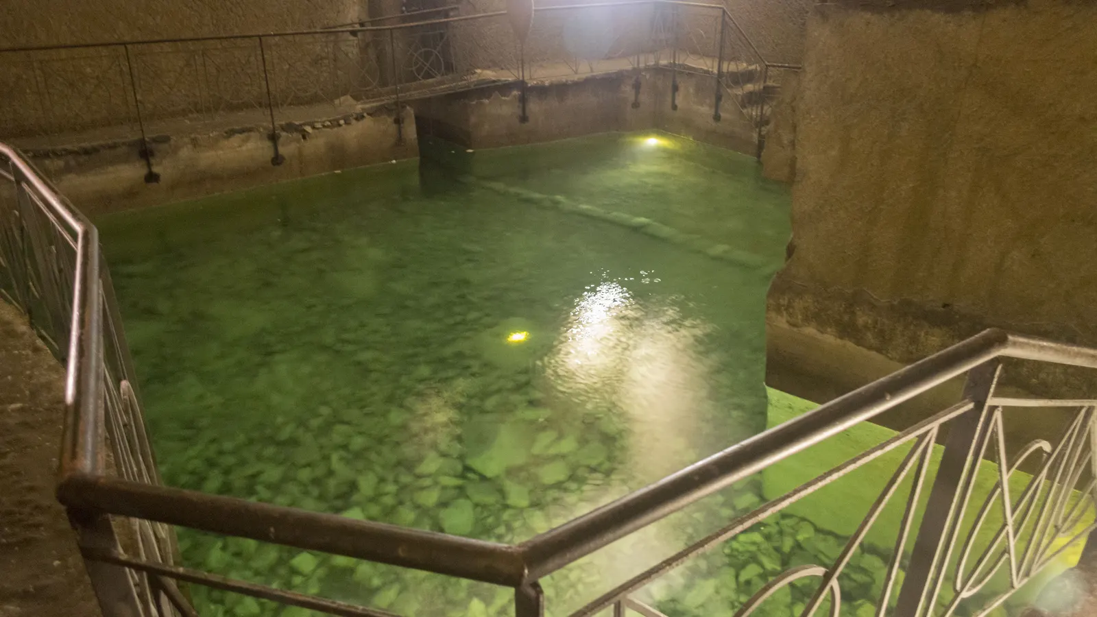 Grün beleuchtete Zisterne mit Geländer im Untergrund von Neapel (Napoli Sotterranea)